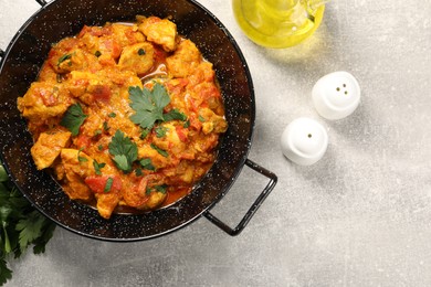 Delicious chicken curry in frying pan, parsley and oil on light grey table, flat lay