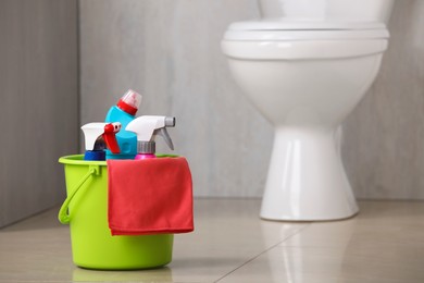 Photo of Bucket with toilet cleaning supplies on floor indoors, space for text