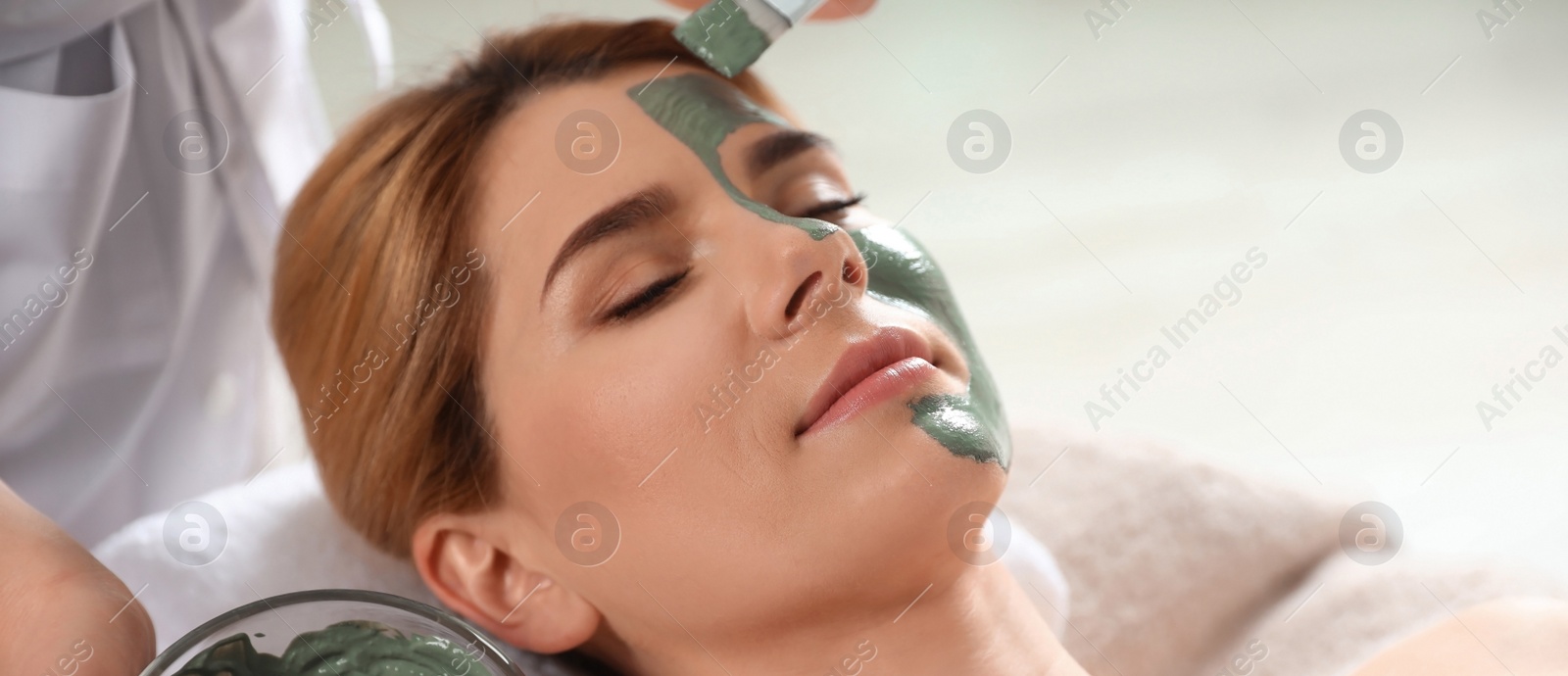 Image of Cosmetologist applying mask onto woman's face in spa salon. Banner design