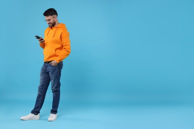 Photo of Handsome young man using smartphone on light blue background, space for text