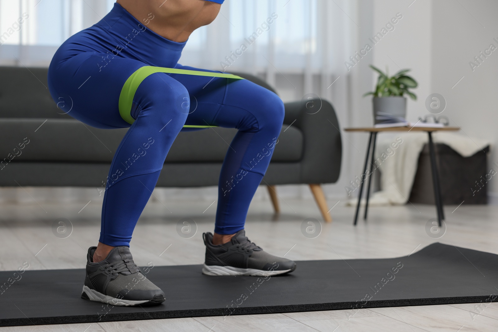 Photo of Woman doing squats with fitness elastic band on mat at home, closeup