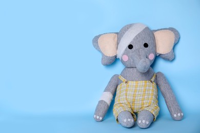 Toy elephant with bandages on light blue background. Space for text