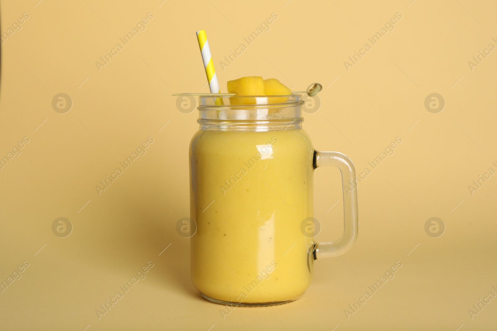 Photo of Mason jar of tasty smoothie with straw and mango on beige background