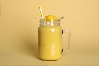 Mason jar of tasty smoothie with straw and mango on beige background