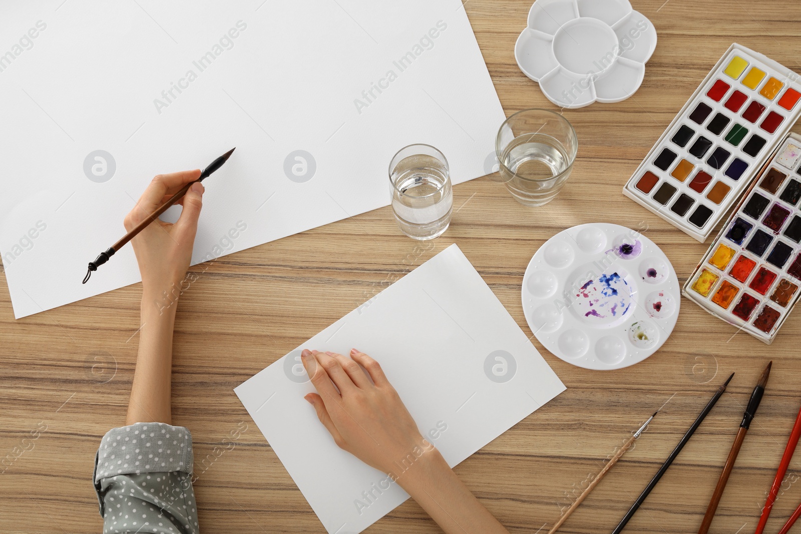 Photo of Woman painting with watercolor on blank paper at wooden table, top view