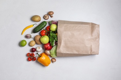 Photo of Paper bag with fresh vegetables and fruits on light background, flat lay