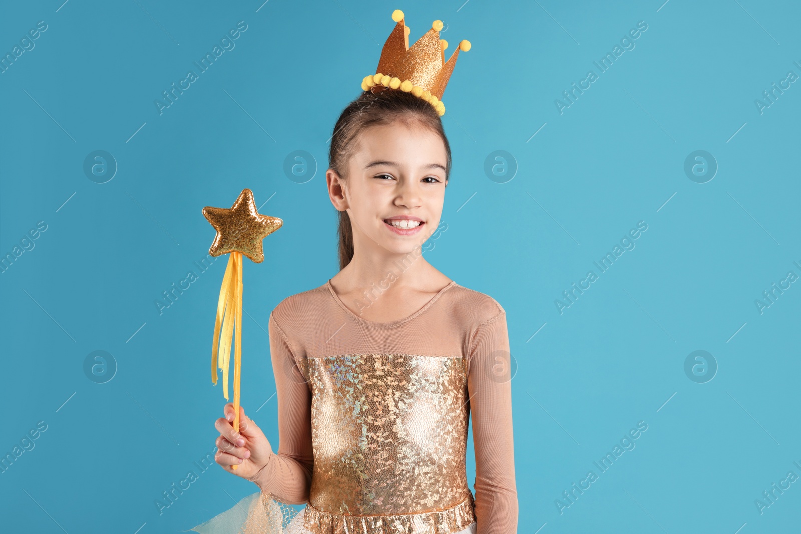 Photo of Cute girl in fairy dress with golden crown and magic wand on light blue background. Little princess
