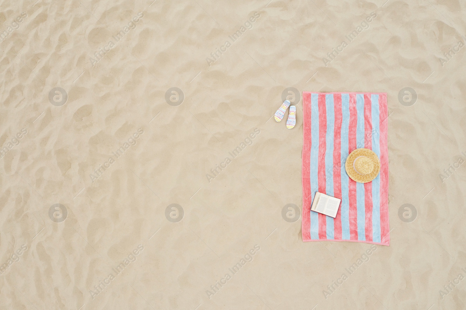 Image of Striped beach towel, book, straw hat and flip flops on sand, aerial view. Space for text