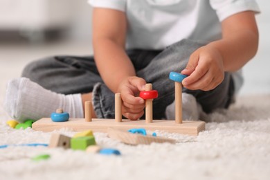 Photo of Motor skills development. Little boy playing with stacking and counting game on floor indoors, closeup