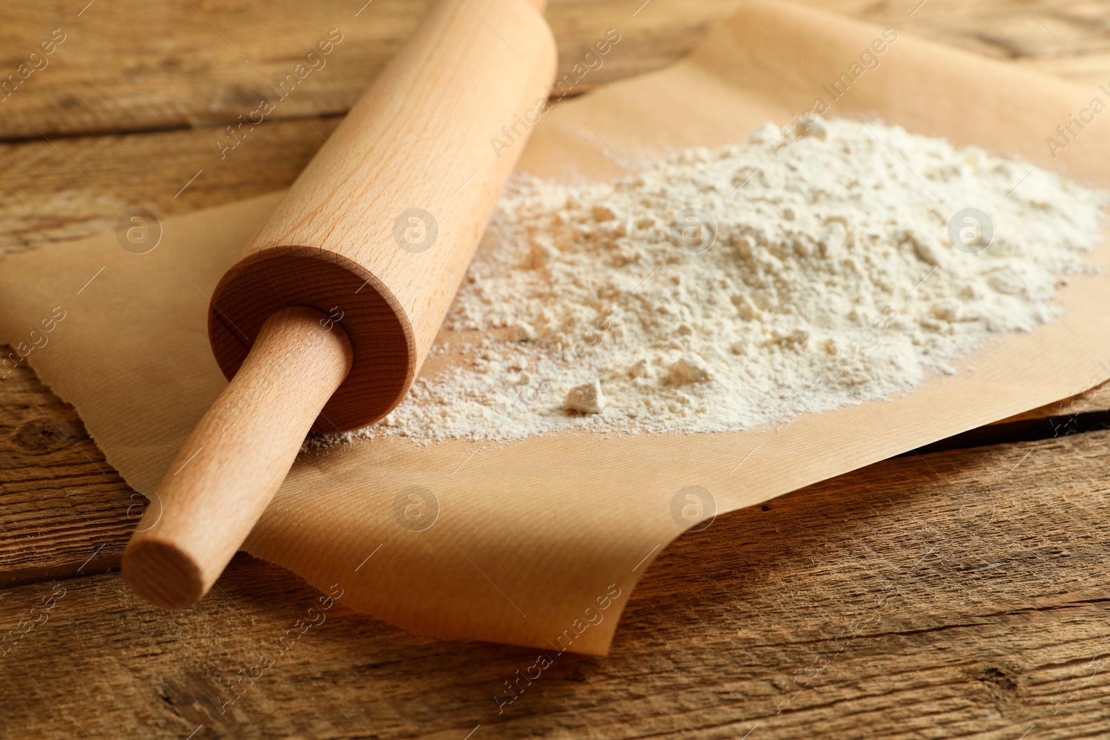 Photo of Parchment with flour and rolling pin on wooden table, closeup