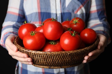 Woman with basket of ripe tomatoes on black background, closeup