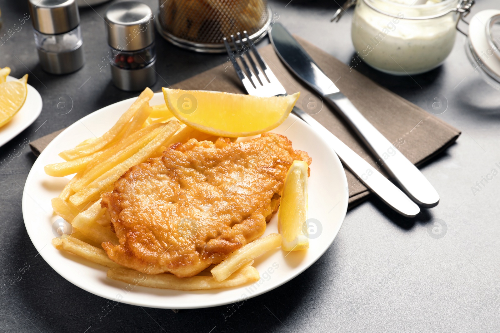 Photo of Plate with British traditional fish and potato chips on grey table