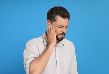 Man suffering from ear pain on light blue background