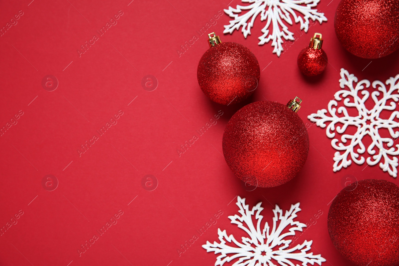Photo of Christmas balls and decorative snowflakes on red background, flat lay. Space for text