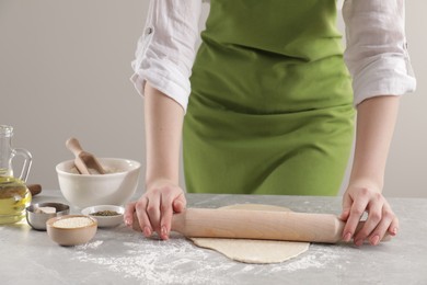 Photo of Woman rolling fresh dough at light grey marble table, closeup. Cooking grissini