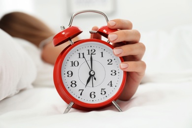 Woman turning off alarm clock in bedroom