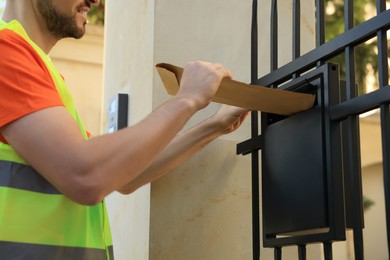 Courier in uniform dropping package into mailbox outdoors, closeup