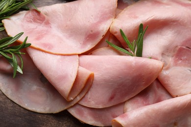Slices of delicious ham and rosemary on wooden table, flat lay