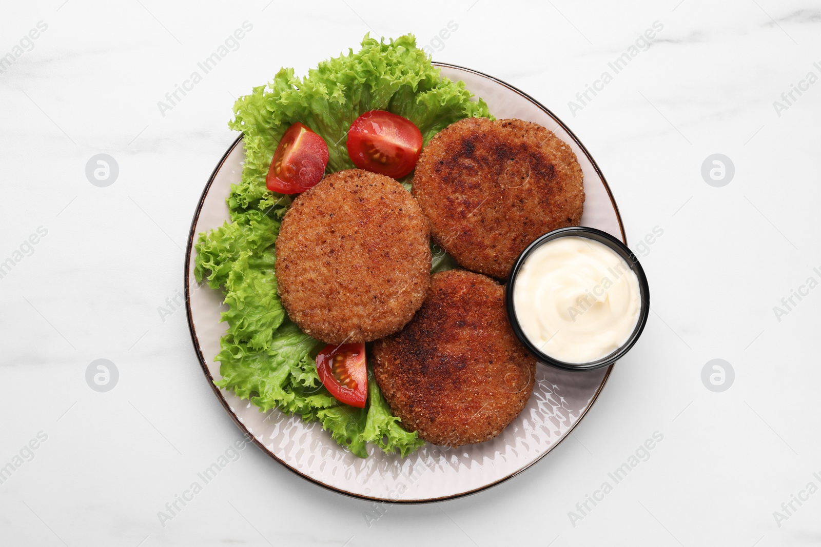 Photo of Plate with delicious vegan cutlets, lettuce, tomatoes and sauce on white marble table, top view