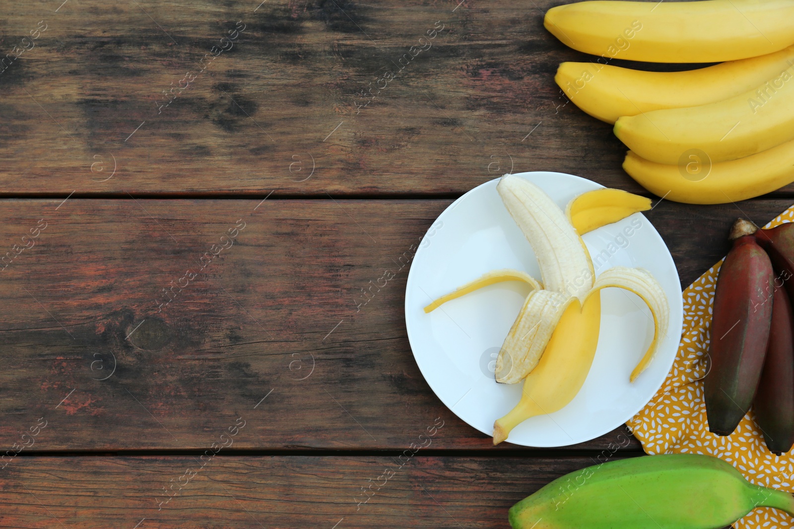 Photo of Many different bananas on wooden table, flat lay. Space for text