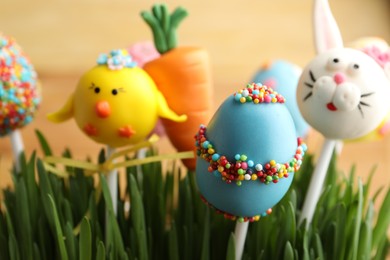 Photo of Delicious sweet cake pops in green grass, closeup. Easter holiday