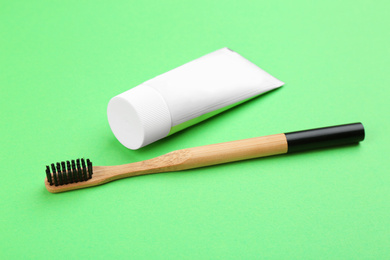 Photo of Natural bamboo toothbrush and paste on green background