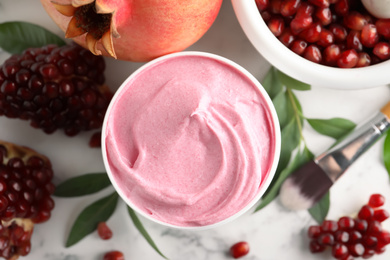 Photo of Fresh pomegranate and jar of facial mask on white marble table, flat lay. Natural organic cosmetics