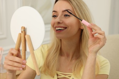 Beautiful woman with mirror applying mascara at home
