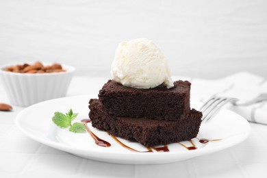 Tasty brownies served with ice cream and caramel sauce on white tiled table, closeup