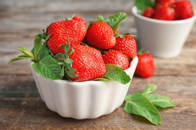 Photo of Bowl with ripe red strawberries and mint on wooden table