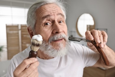 Photo of Man shaving mustache and beard with blade in bathroom