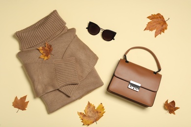 Sweater, bag and sunglasses with dry leaves on yellow background, flat lay. Autumn season