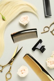 Flat lay composition with professional hairdresser tools, flowers and blonde hair strand on light grey background
