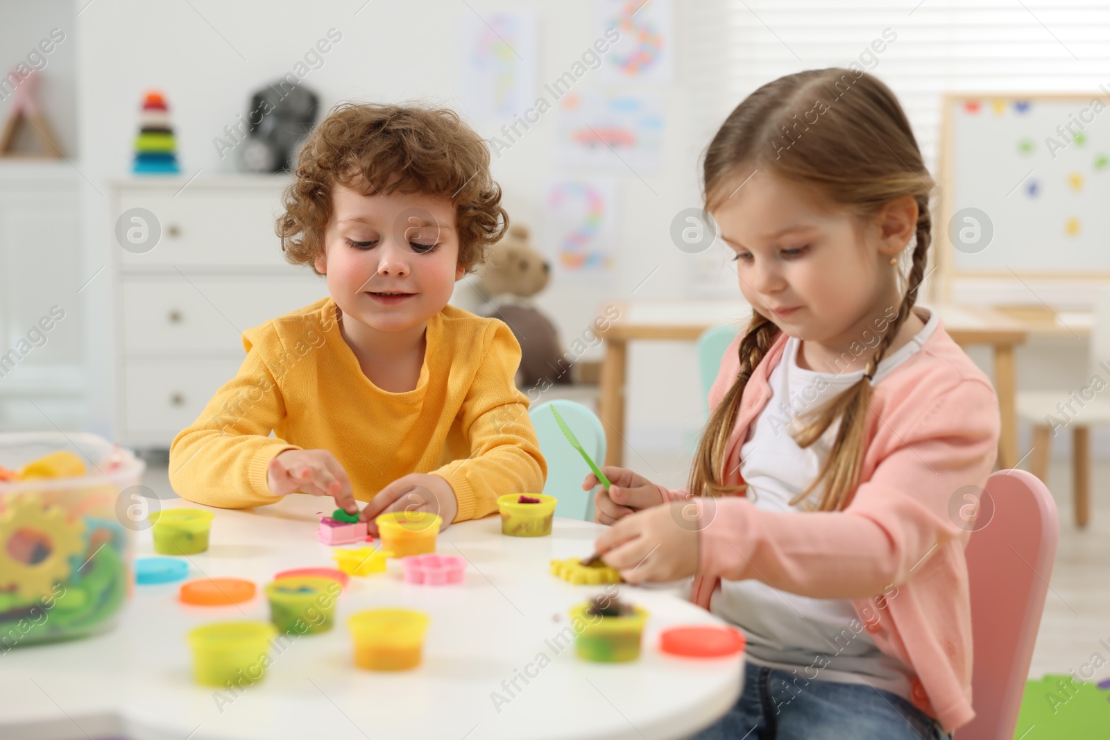 Photo of Cute little children modeling from plasticine at white table in kindergarten