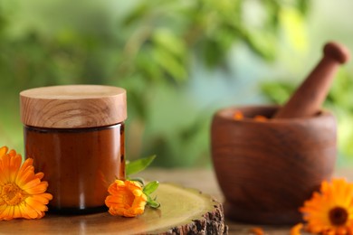 Photo of Jar of cosmetic product and beautiful calendula flowers on wooden stump outdoors, space for text
