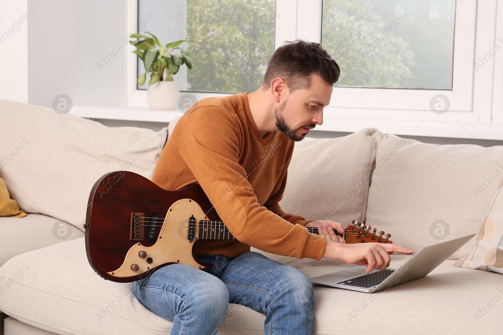 Photo of Man learning to play guitar with online music course at home. Time for hobby