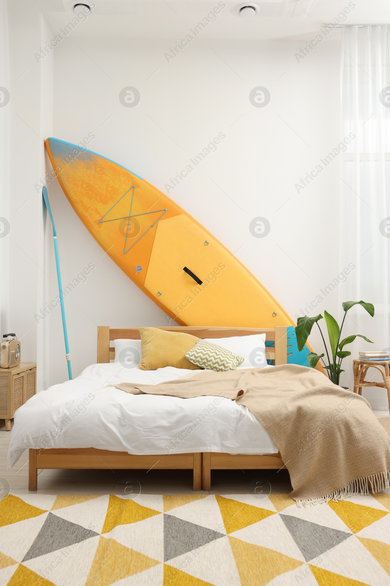 Photo of Large comfortable bed, SUP board and green houseplant in stylish bedroom. Interior design