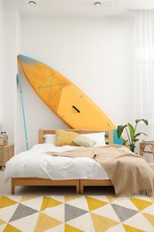 Large comfortable bed, SUP board and green houseplant in stylish bedroom. Interior design