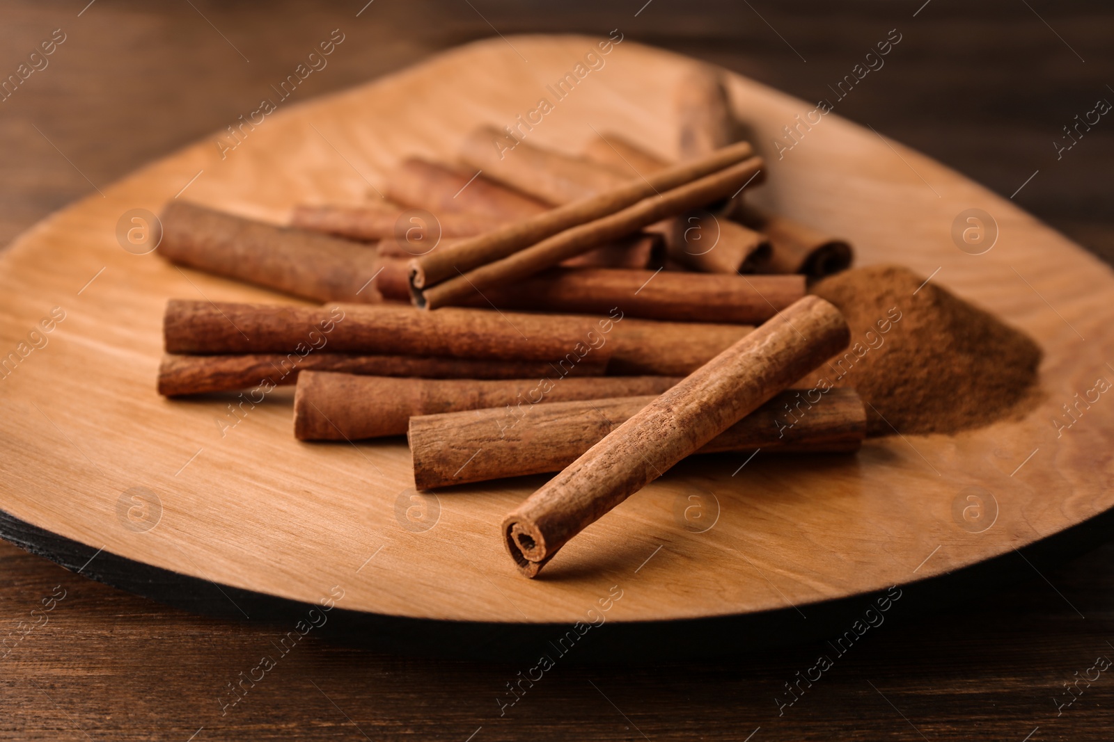 Photo of Plate with aromatic cinnamon powder and sticks on wooden table