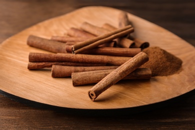 Plate with aromatic cinnamon powder and sticks on wooden table