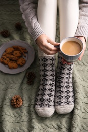 Photo of Woman relaxing with cup of hot winter drink on knitted plaid, closeup. Cozy season