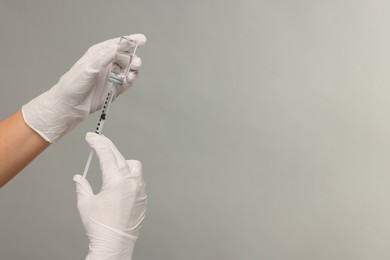 Photo of Doctor filling syringe with medication from glass vial on grey background, closeup. Space for text