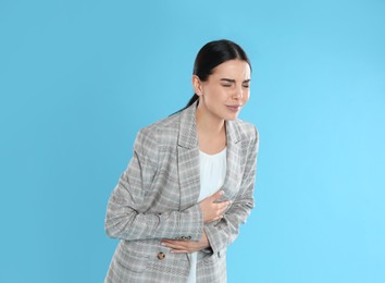 Woman in office suit suffering from stomach ache on light blue background Food poisoning