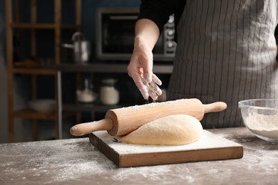 Photo of Woman sprinkling flour over dough on table in kitchen