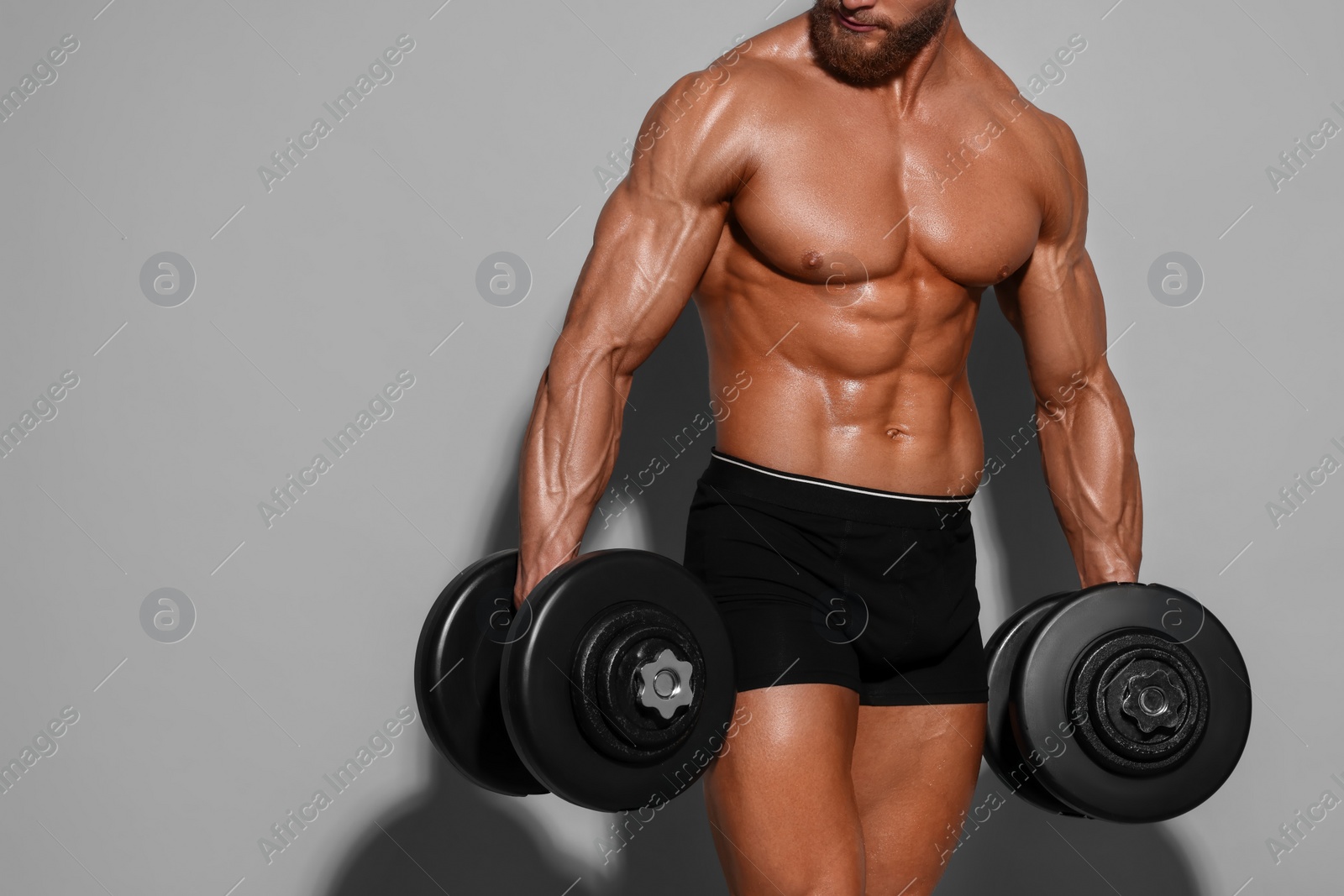 Photo of Young bodybuilder exercising with dumbbells on light grey background, closeup. Space for text