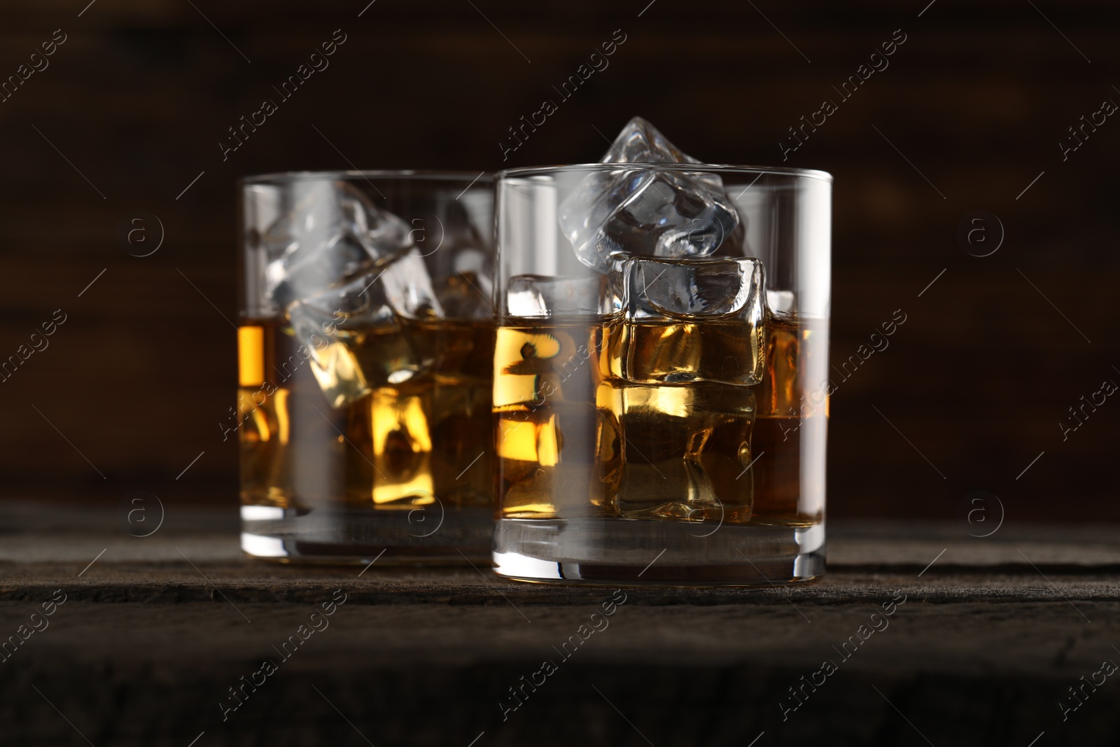 Photo of Whiskey with ice cubes in glasses on wooden table, closeup