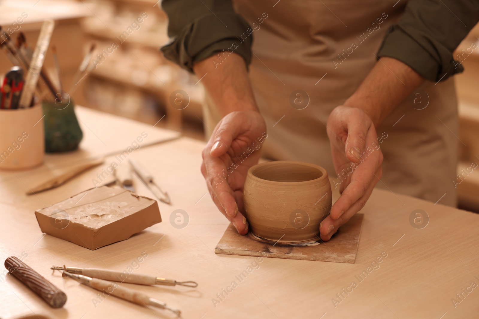 Photo of Clay crafting. Man making bowl at table indoors, closeup