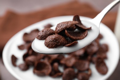 Photo of Breakfast cereal. Eating chocolate corn flakes and milk with spoon from bowl on table, closeup