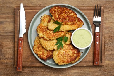 Tasty parsnip cutlets with parsley and sauce served on wooden table, top view