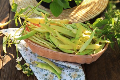 Photo of Wicker basket with fresh green beans on wooden table in garden